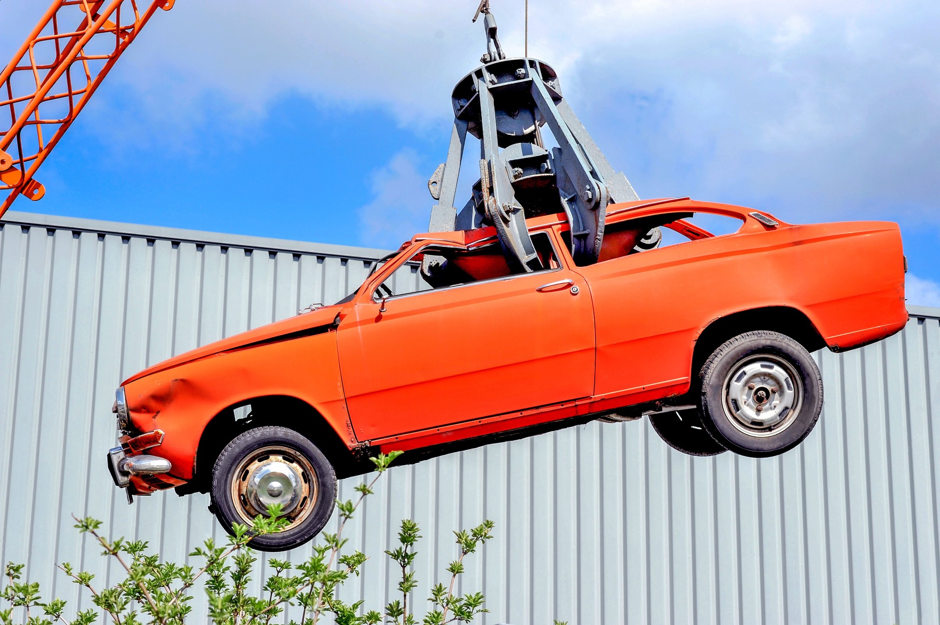 Red vintage car wreck on the hook in a junkyard ready for the scrap press hanging in the air with blue sky